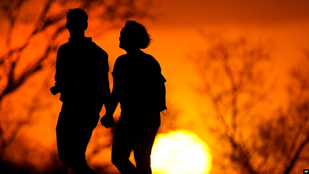In this file photo, a couple walks through a park at sunset, March 10, 2021, in Kansas City, Mo. (AP Photo/Charlie Riedel, File)