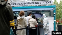 5月6日，北京市民冒雨在一流動新冠病毒核酸檢測站前排隊等候檢測，一名身穿防護服的工作人員在維持秩序。 -路透社照