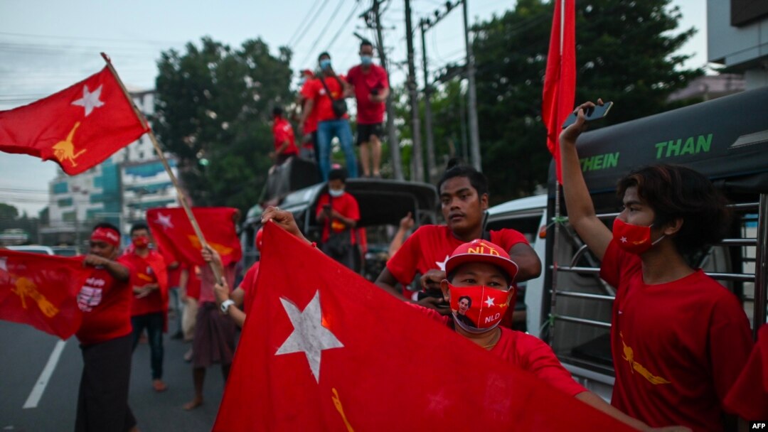 Supporters of the National League for Democracy (NLD) party wave flags in front of the party's headquarters in Yangon on November 9, 2020, as NLD officials said they were confident of a landslide victory in the weekend's election. (Photo by Ye Aung Thu / 