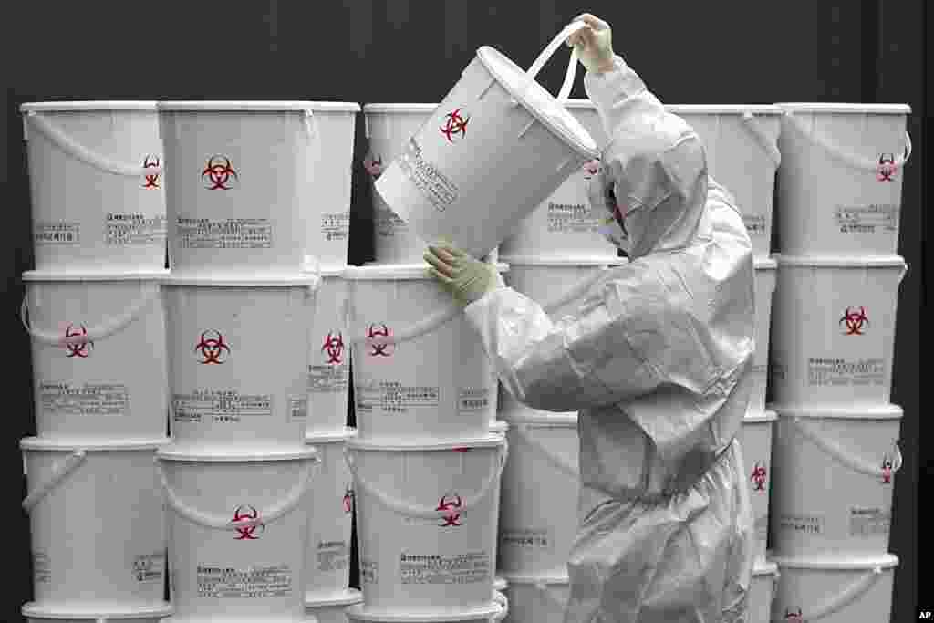 A worker in protective gear stacks plastic buckets containing medical waste from coronavirus patients at a medical center in Daegu, South Korea.