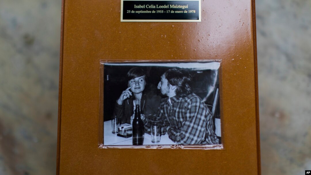 Esta foto muestra una urna de madera que contiene los restos óseos de Isabel Loedel, quien fue desaparecida durante la dictadura argentina, adornada con una imagen de ella y su compañero Julio Di Giacinti en 1976.