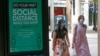 FILE - Two women walk past a social distance sign at City Creek Center in Salt Lake City, Utah, May 6, 2020.