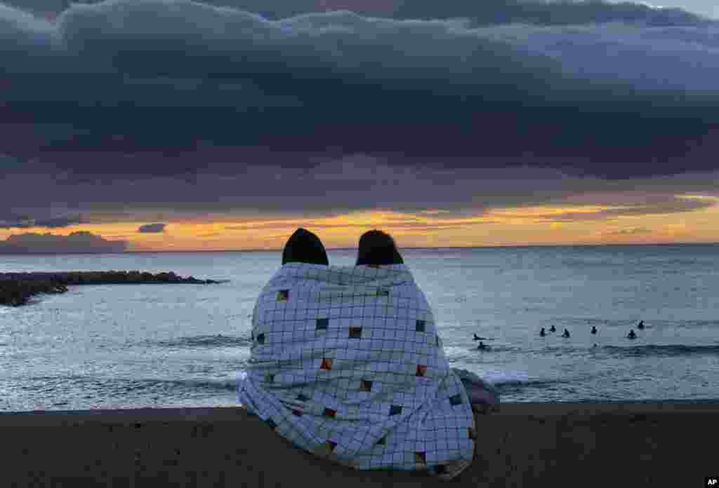 Sepasang kekasih menyaksikan matahari terbit di pantai Laut Mediterania di Barcelona, Spanyol, Minggu, 24 Januari 2021. (Foto: AP) 