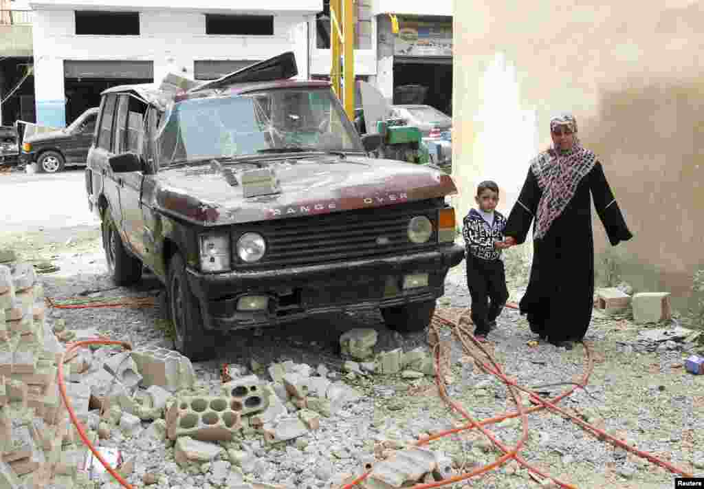 People walk next to a vehicle damaged by what residents say was a missile fired by Syrian rebels in the town of Hermel in Bekaa, April 24, 2013.