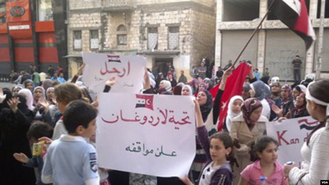 Niños y mujeres sirios pueden ser vistos en la foto tomada por ciudadanos con teléfonos celulares, con carteles donde reclaman la salida de al-Assad del poder.