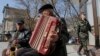 A member of a pro-Russian self-defence unit walks past street musicians in the Crimean city of Simferopol April 7, 2014. 