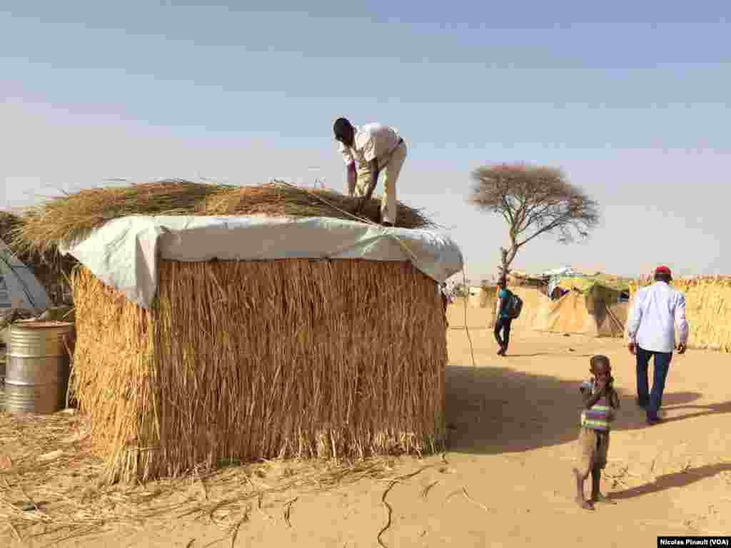 A humanitarian worker places straw on the roof of a hut at the Assaga camp, Diffa, Feb. 29, 2016. (N. Pinault/VOA)