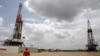 ARCHIVO - Un trabajador petrolero camina junto a plataformas de perforación en un pozo operado por la petrolera estatal venezolana PDVSA, en la faja petrolera del Orinoco, rica en petróleo, el 16 de abril de 2015.