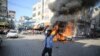Um palestiniano celebra junto a um carro civil israelita em chamas retirado do kibutz de Kfra Azza em Beit Lahiya, Faixa de Gaza, sábado, 7 de outubro de 2023. Militantes do Hamas levaram a cabo um ataque sem precedentes, com várias frentes, contra Israel ao amanhecer de sábado