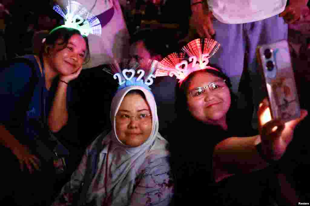 Mulheres que usam faixas '2025' tiram selfies durante as celebrações da véspera de Ano Novo em Jacarta, Indonésia, a 31 de dezembro de 2024.