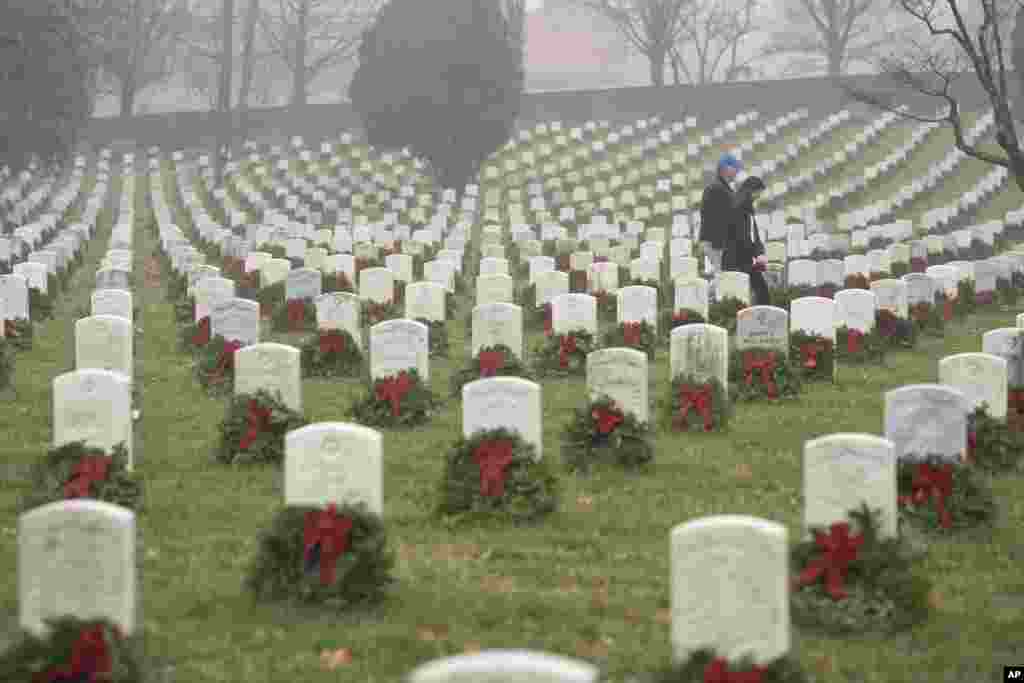 People walk among headstones with holiday wreaths in Arlington National Cemetery during Wreaths Across America Day in Arlington, Virginia, Dec. 14, 2019.