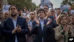 El vicepresidente catalán, Oriol Junqueras (izquierda), el presidente catalán, Carlos Puigdemont (segundo desde la izquierda) y Carne Forcadell, líder de la Cámara del Parlamento catalán aplauden durante una manifestación contra la decisión de Madrid el sábado, 21 de octubre de 2017.