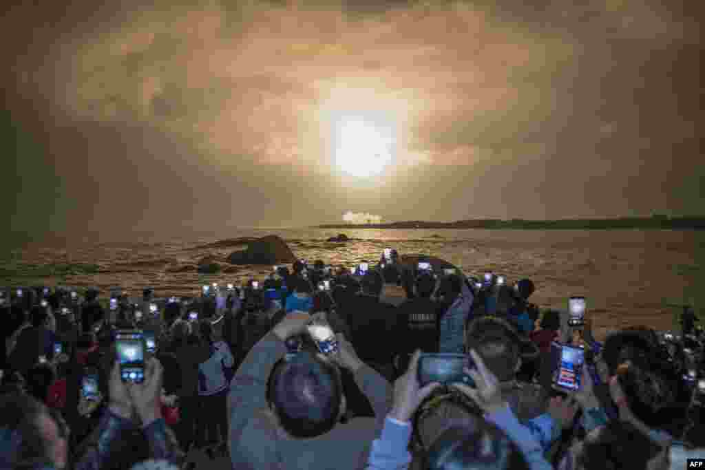 People take photos as China's heavy-lift Long March 5 rocket blasts off from its launch center in Wenchang, south China's Hainan province.