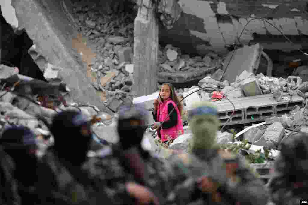 A child walks amid the wreckage of a building as Palestinian fighters from the armed wing of Hamas take part in the funeral procession of Marwan Issa, a top Hamas commander killed in March 2024, in the war-devastated Bureij refugee camp in the central Gaza Strip.