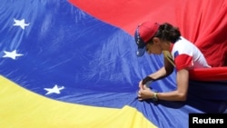 Un partidario del líder de la oposición venezolana Juan Guaidó, remienda una bandera durante una manifestación contra el gobierno del presidente Nicolás Maduro, el 6 de abril de 2019. [Foto: Reuters]