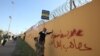 ARCHIVO - Un miembro de un grupo paramilitar chiíta iraquí ayuda a otro manifestante que sostiene una pancarta en el muro exterior de la embajada estadounidense en la Zona Verde de Bagdad el 31 de diciembre de 2019.