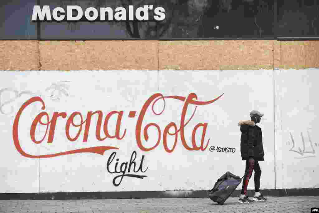 A man walks past a graffiti on a wall of a closed McDonald's fast restaurant, reading "Corona Cola light", in Nantes, western France, March 17, 2020 while a strict lockdown comes into effect to stop the spread of the COVID-19 in the country.