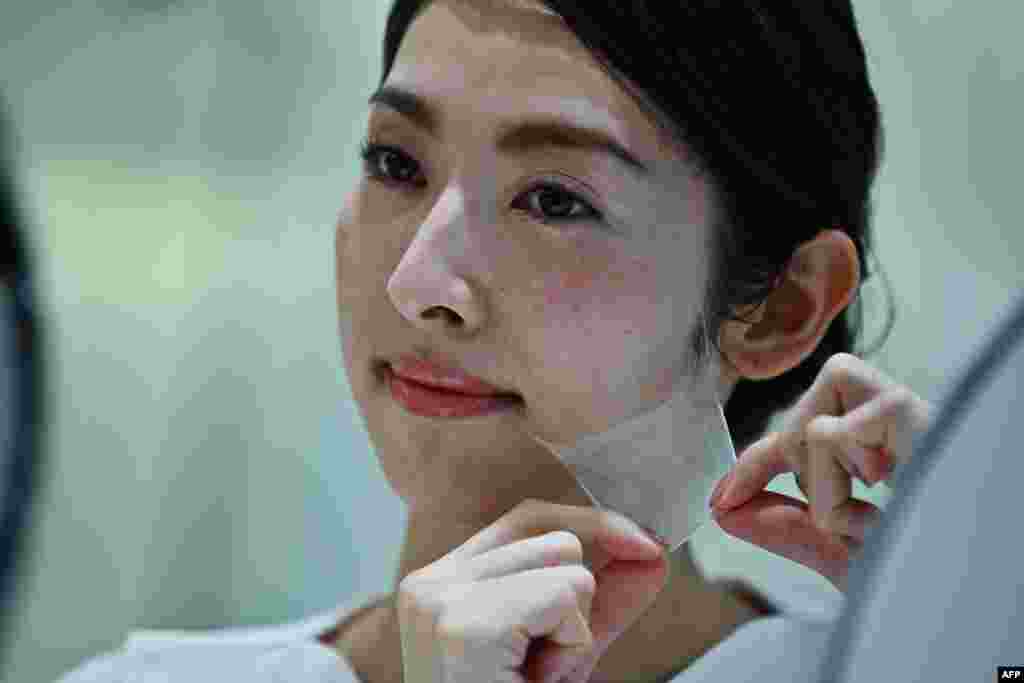 An employee for Japanese cosmetics company Kao removes a super thin transparent layer after using a palm-sized diffuser on her face, during a product demonstration in Tokyo, Dec. 4, 2019. The company unveiled what it said was the world's first spray-on skin, using fibers one-100th the thickness of a human hair to form a membrane covering the face.