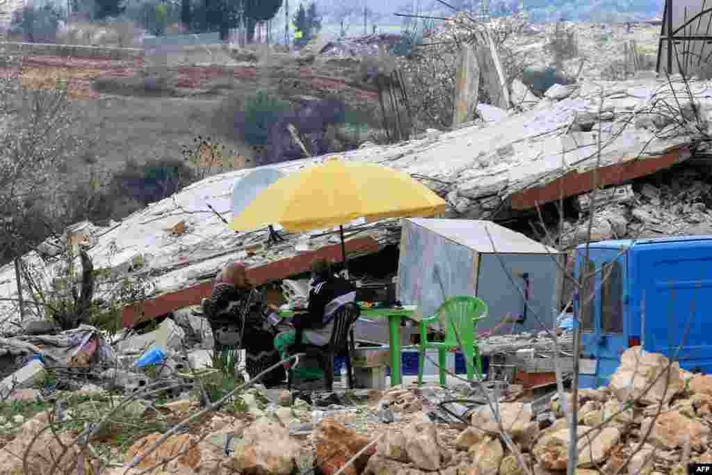 People sit around a table atop the wreckage of their house, destroyed during the recent war between Israel and Hezbollah, in the village of al Jibbain in southern Lebanon.