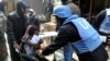 UN relief worker gives food supplies to Palestinian woman at the gate of the besieged Yarmouk refugee camp, Damascus, Feb. 4, 2014.