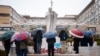 Pessoas rezam debaixo de chuva junto à estátua de João Paulo II no Hospital Universitário Gemelli, onde o Papa Francisco está hospitalizado com pneumonia, em Roma, a 1 de março de 2025.